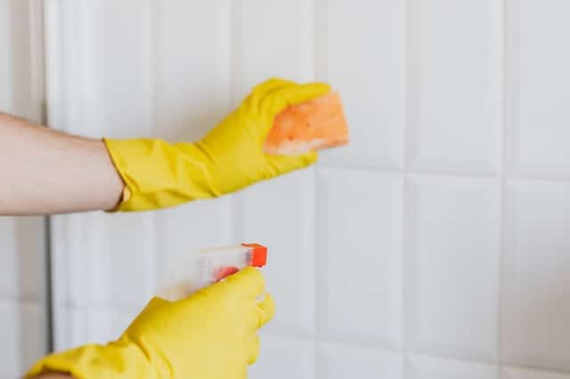 Cleaning tiles with yellow gloves and sponge