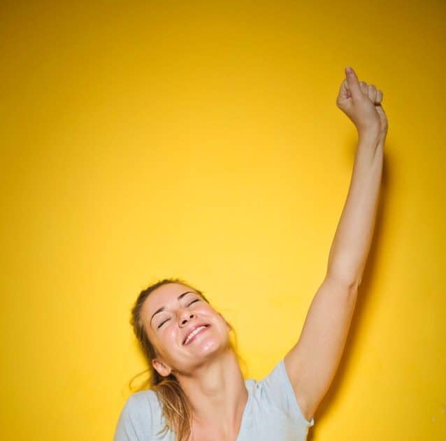Happy woman with arm raised triumphantly in front of yellow wall